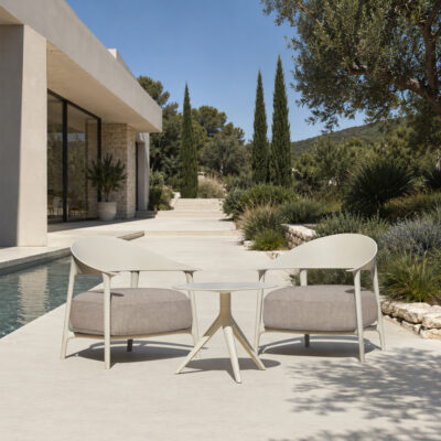 Modern outdoor seating area with two curved lounge chairs and a small table between them beside a pool in a landscaped yard.