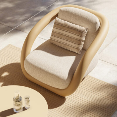 Beige cushioned lounge chair with a curved frame, placed on a wooden outdoor rug next to a round table with glasses on it.