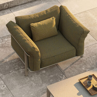 Olive-green cushioned armchair with a matching pillow on a stone patio, beside a wooden tray with cups.