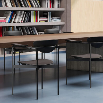 Long wooden table with black metal chairs in a modern library or reading room, bookshelves in the background.