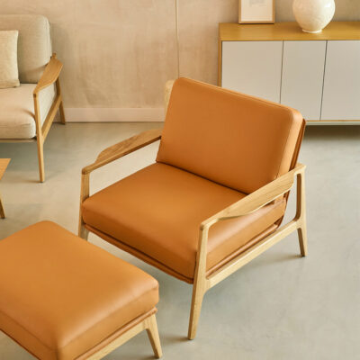 Tan leather armchair with a matching ottoman and light wood frame in a minimalist living room.