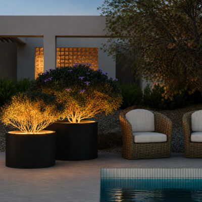 Illuminated potted trees with purple flowers flanking a modern outdoor seating area by a pool at dusk.