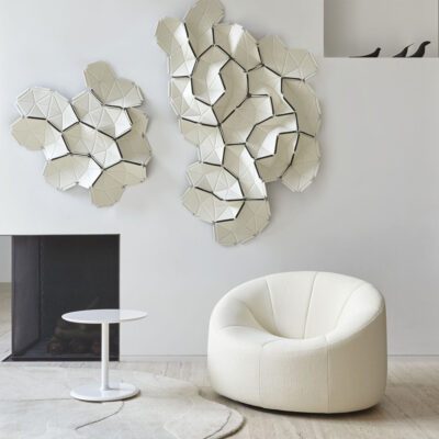 Modern living room corner with white geometric wall sculpture, a round white side table, and a cream curved armchair.